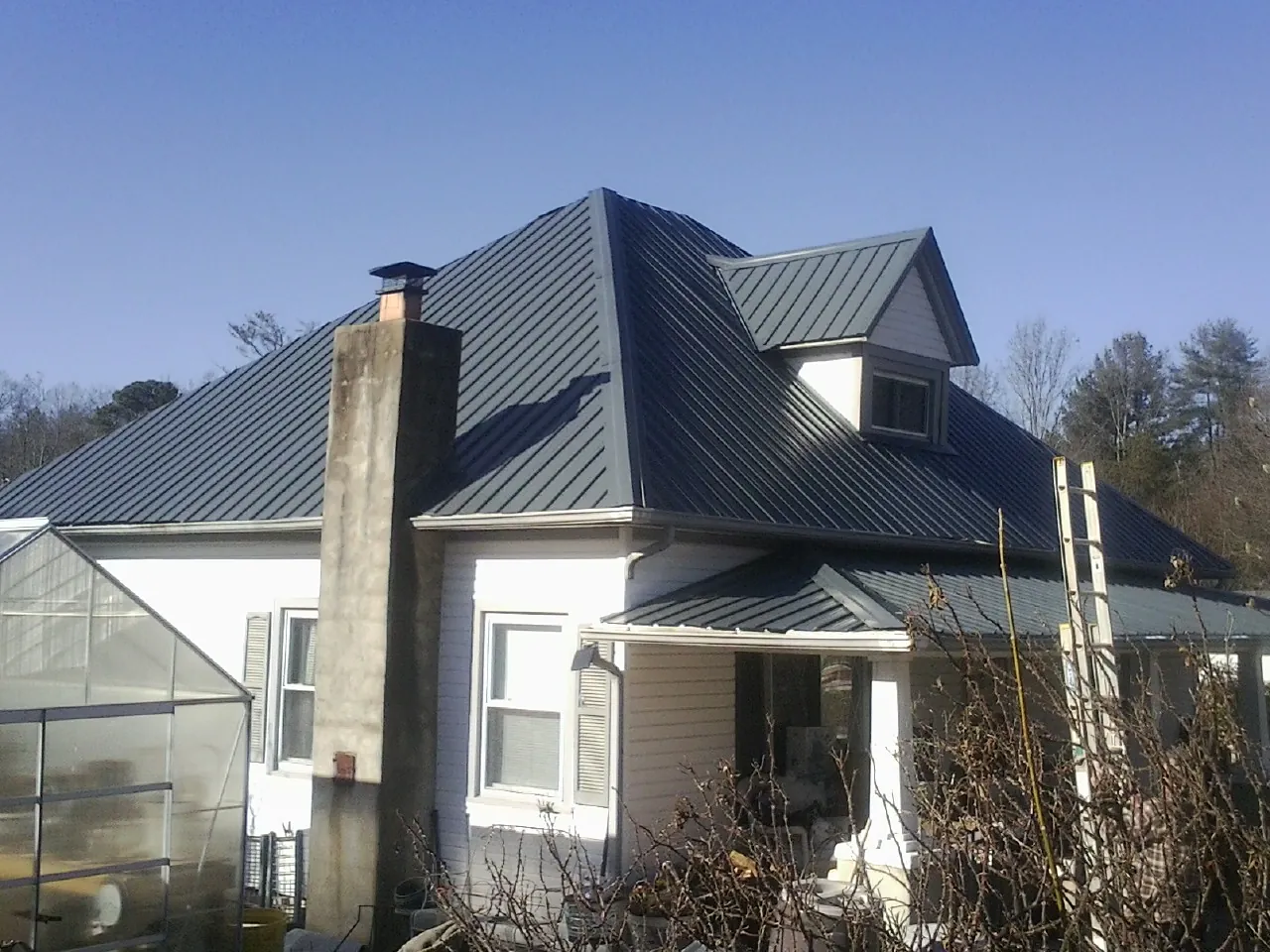 Dark blue standing seam metal roof on a white farmhouse with dormer — Slate & Tile Roof Repair by Roofing Brothers in Rensselaer