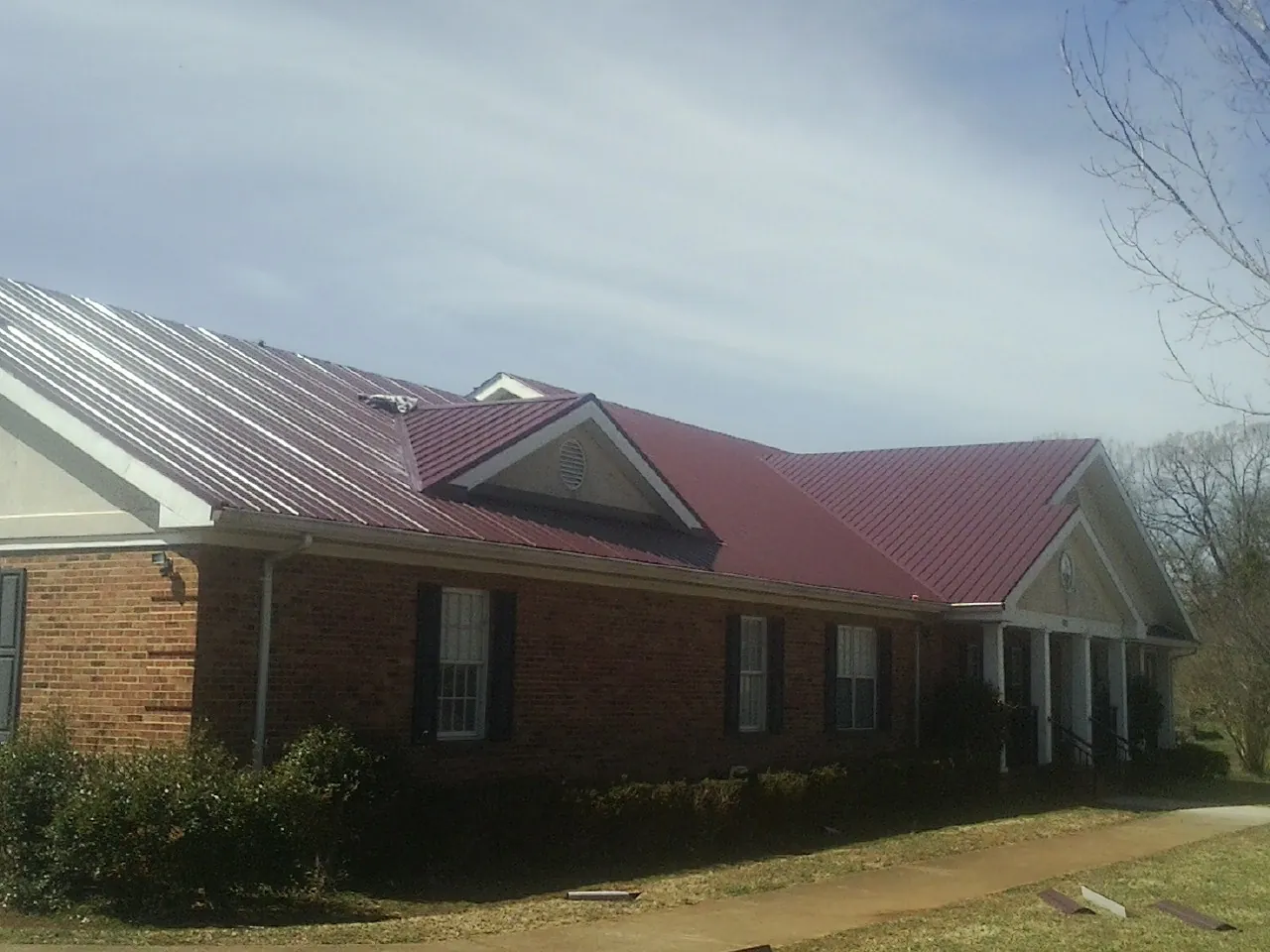 Red metal roof with gabled entries on a long brick building, from a Hail Damage Roof Repair job in Rensselaer