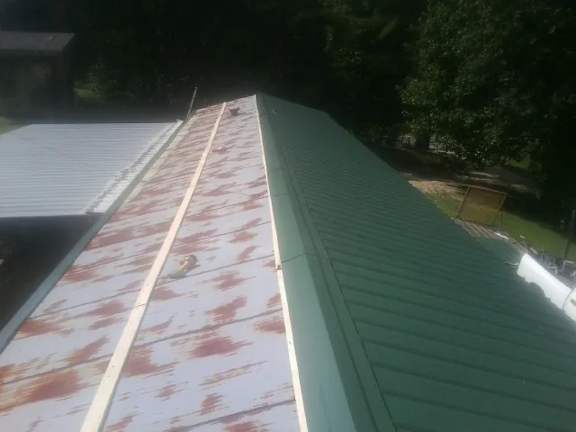 Old rusted panels beside newly installed green metal roofing — Wind Damage Roof Repair by Roofing Brothers in Rensselaer