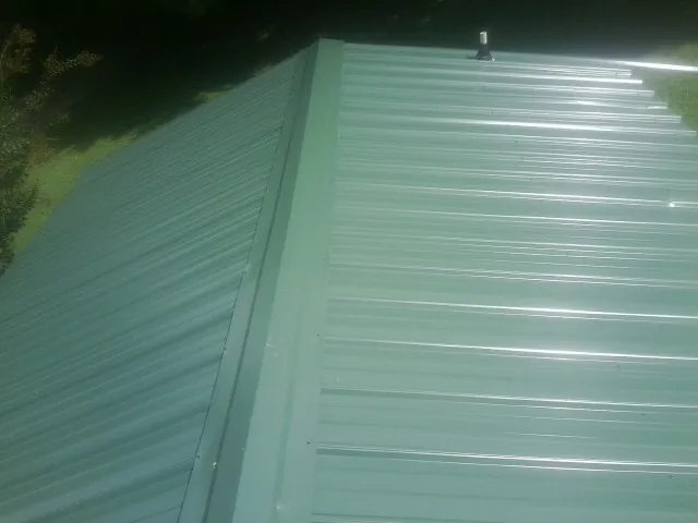 New green metal panels meeting at the ridge of a roof — Flat Roof Repair work by our crew in Rensselaer