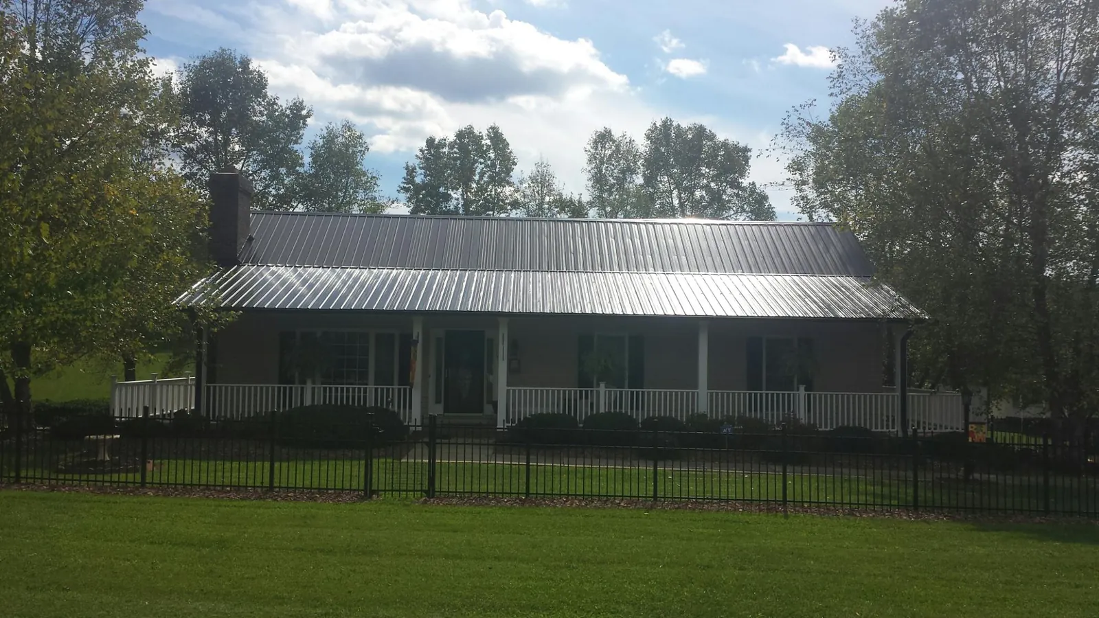 Gray metal roof on a brick ranch with a full width front porch — Gutter Guard Installation work by our crew in Rensselaer