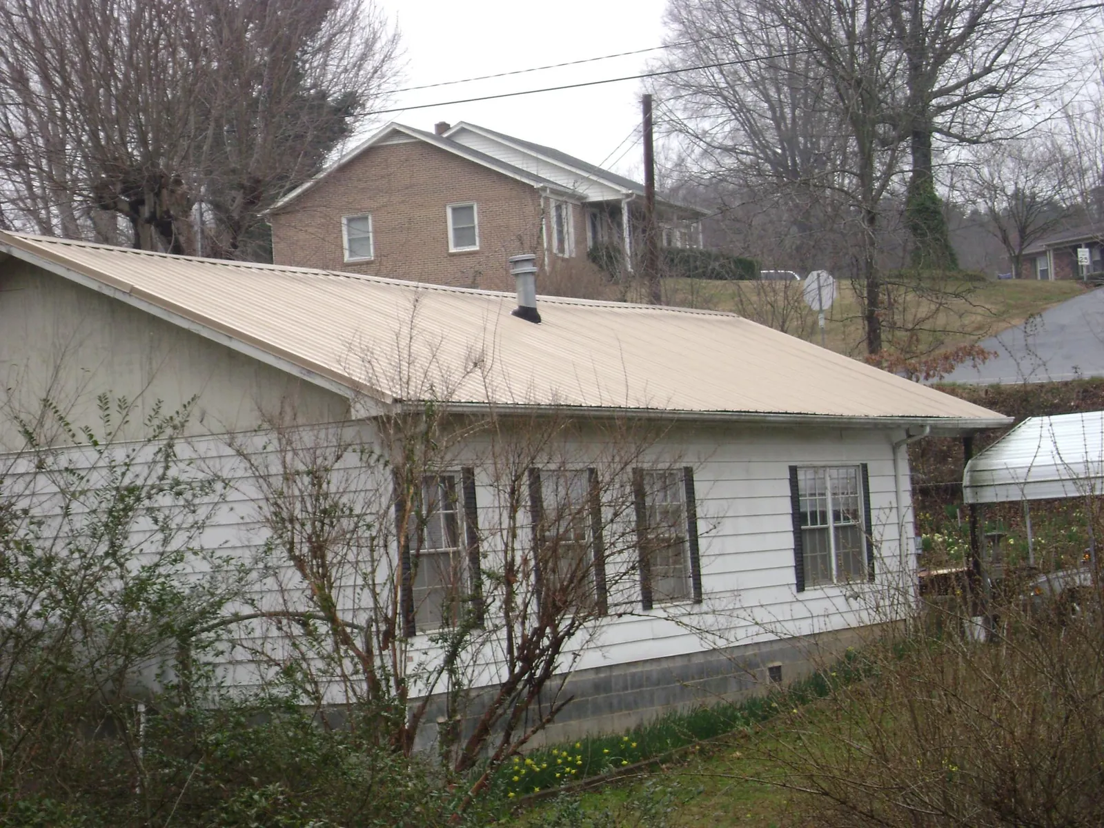 Tan metal roof on a white sided house set into a hillside — Commercial Roofing by Roofing Brothers in Rensselaer
