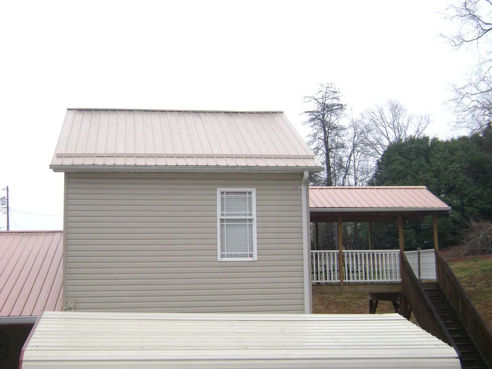 Tan metal roofs on a two story addition and attached porch, from a Roof Replacement job in Rensselaer