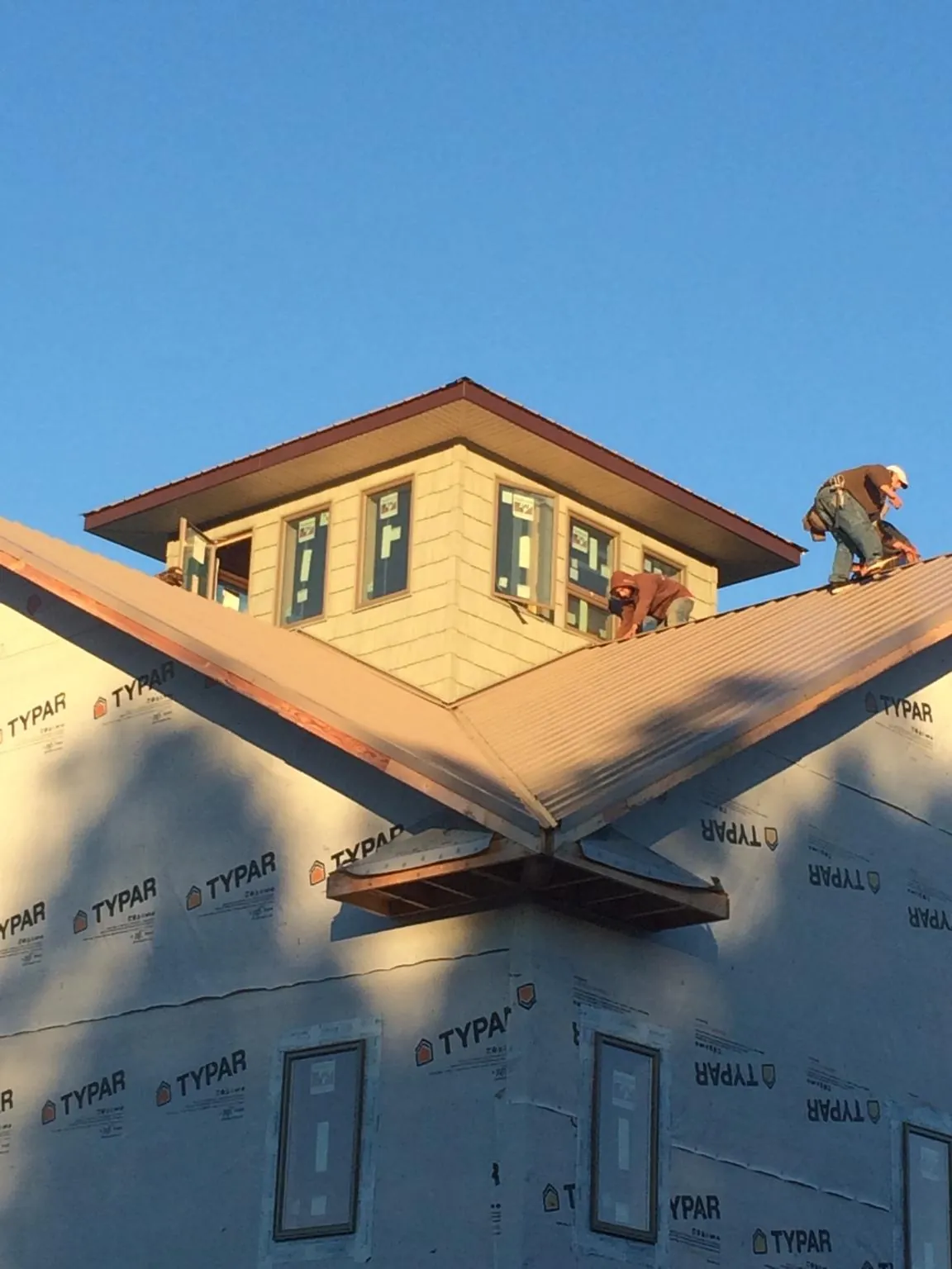 Roofers working around a rooftop cupola on a new metal roof at sunset — Roof Waterproofing in Rensselaer by Roofing Brothers